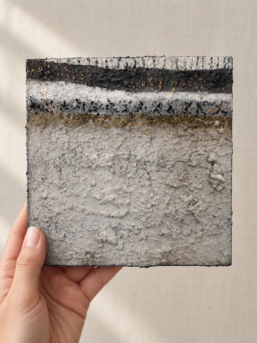 Erdfragment Nr. 1, kleines Wandobjekt 15×15 cm in Schwarz, Weiß und Gold, in der Hand gehalten zum Größenvergleich